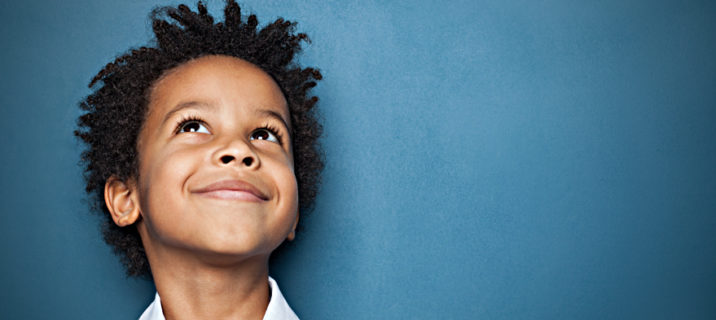 Little black child boy smiling and looking up on blue background